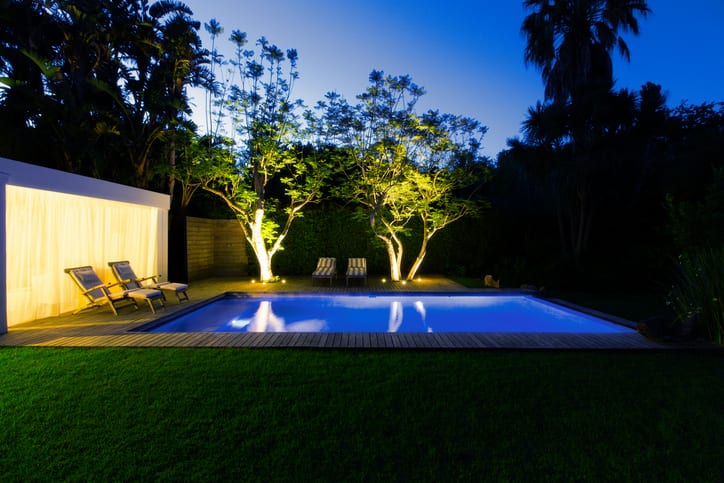Palmetto Electrical Contractors | an illuminated swimming pool at night with lit up landscaping and trees